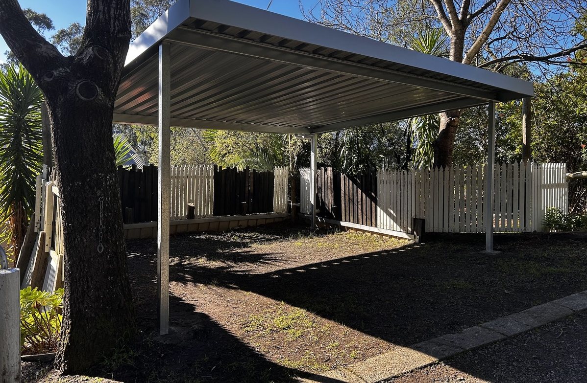 A new double carport with a flat steel roof built over the same yard, after