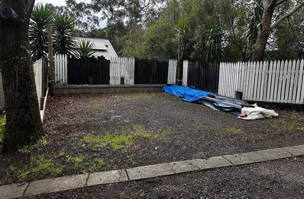 Bare side yard with a gravel surface and stacked materials, before