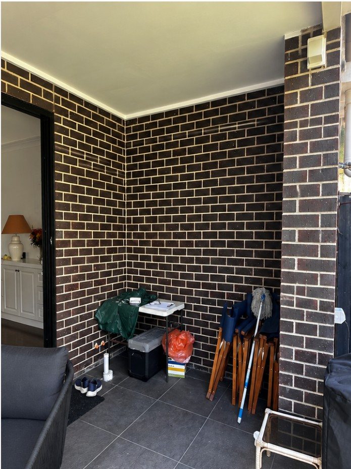 Bare brick alfresco wall cluttered with stored furniture, before